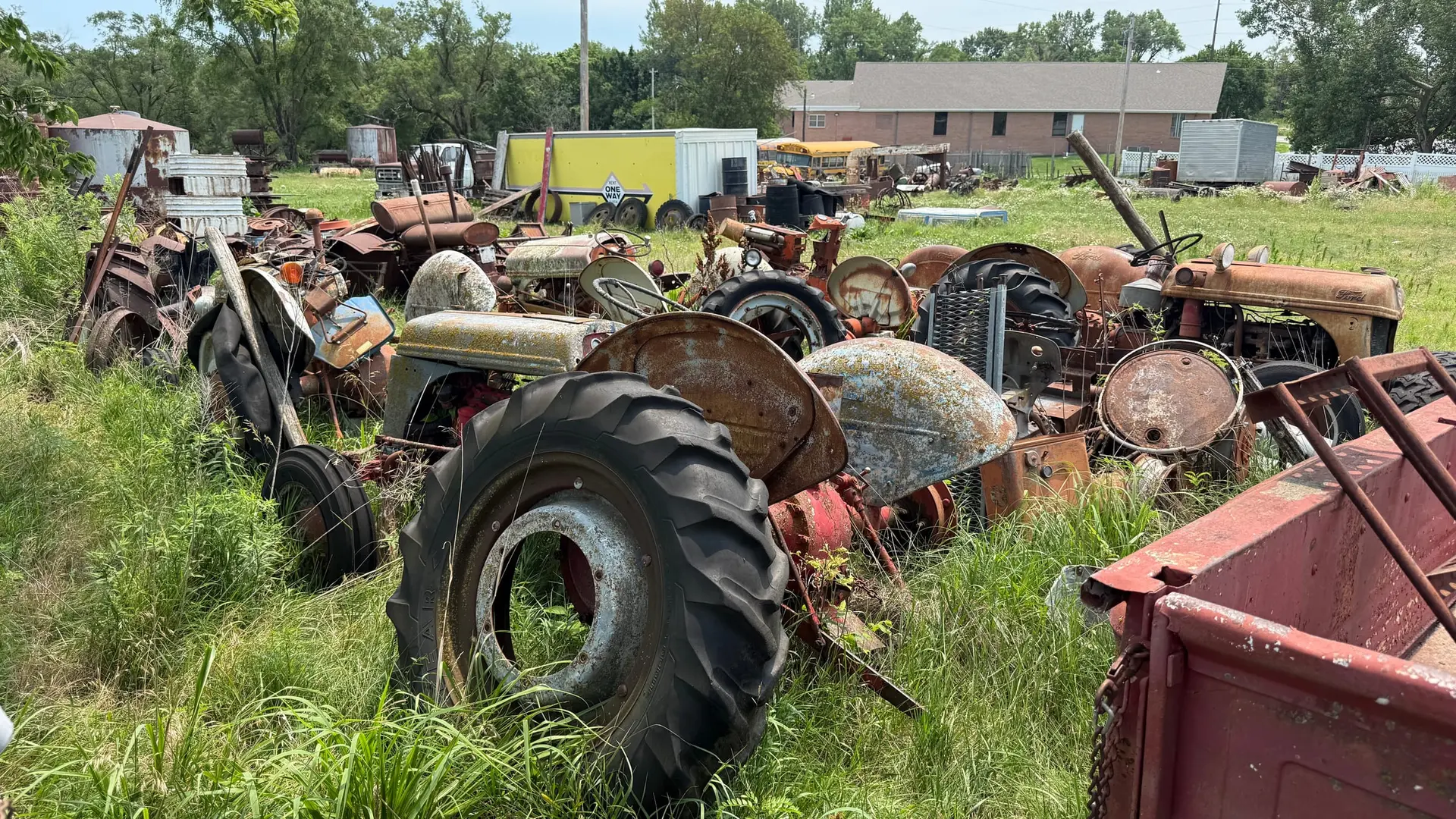 Old tractors and farm equipment crowded together in tall grass