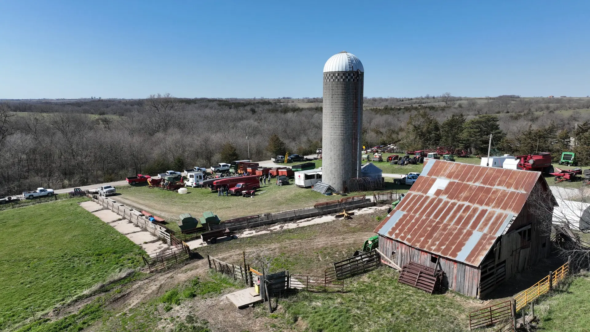 Aerial view of a farm auction with a silo, barn and rows of equipment