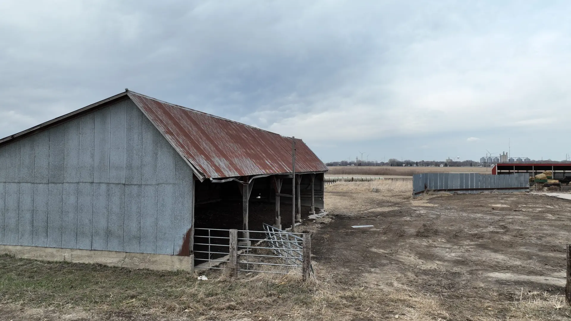 An open-front farm shed beside a lot with farmland stretching behind it